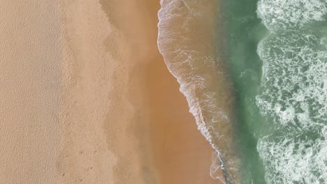 Aerial-top-down-view-of-few-tourists-enjoying-the-landscape-and-sunny-weather-at-the-beach-with-waves-hitting-the-shore