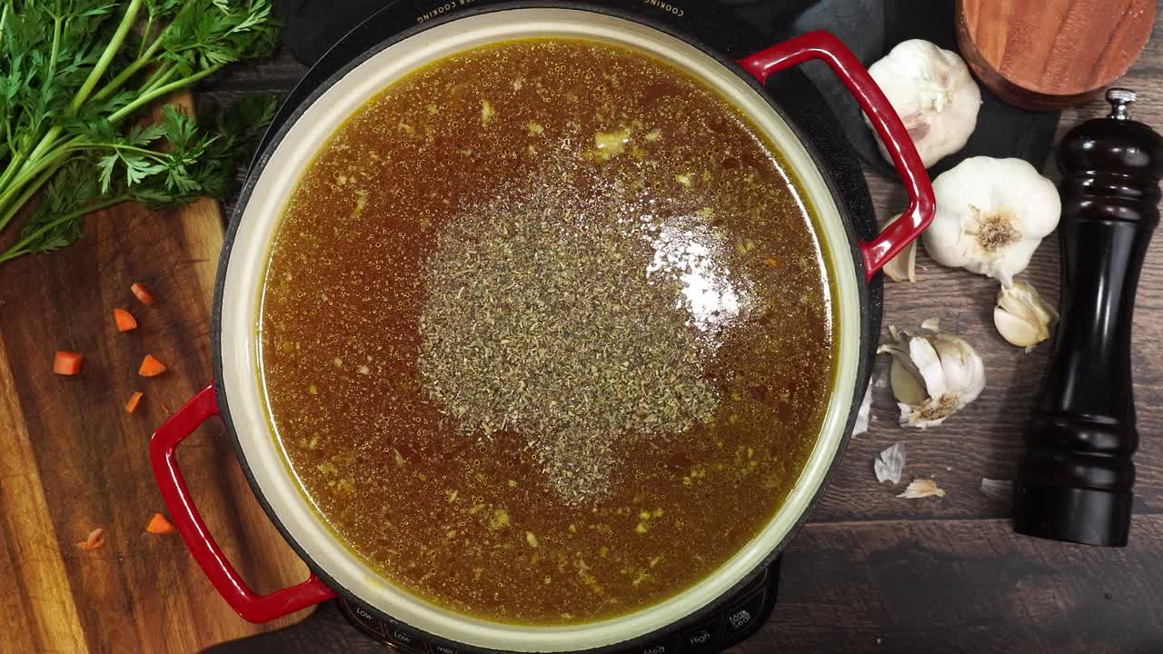 Cooking Italian Wedding Soup and adding spices like oregano or basil to the red stock pot. Mixing in spices and herbs to soup. Using a wooden spoon to stir the broth while simmering soup.