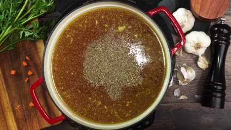 cooking italian wedding soup and adding spices like oregano or basil to the red stock pot. mixing in spices and herbs to soup. using a wooden spoon to stir the broth while simmering soup.