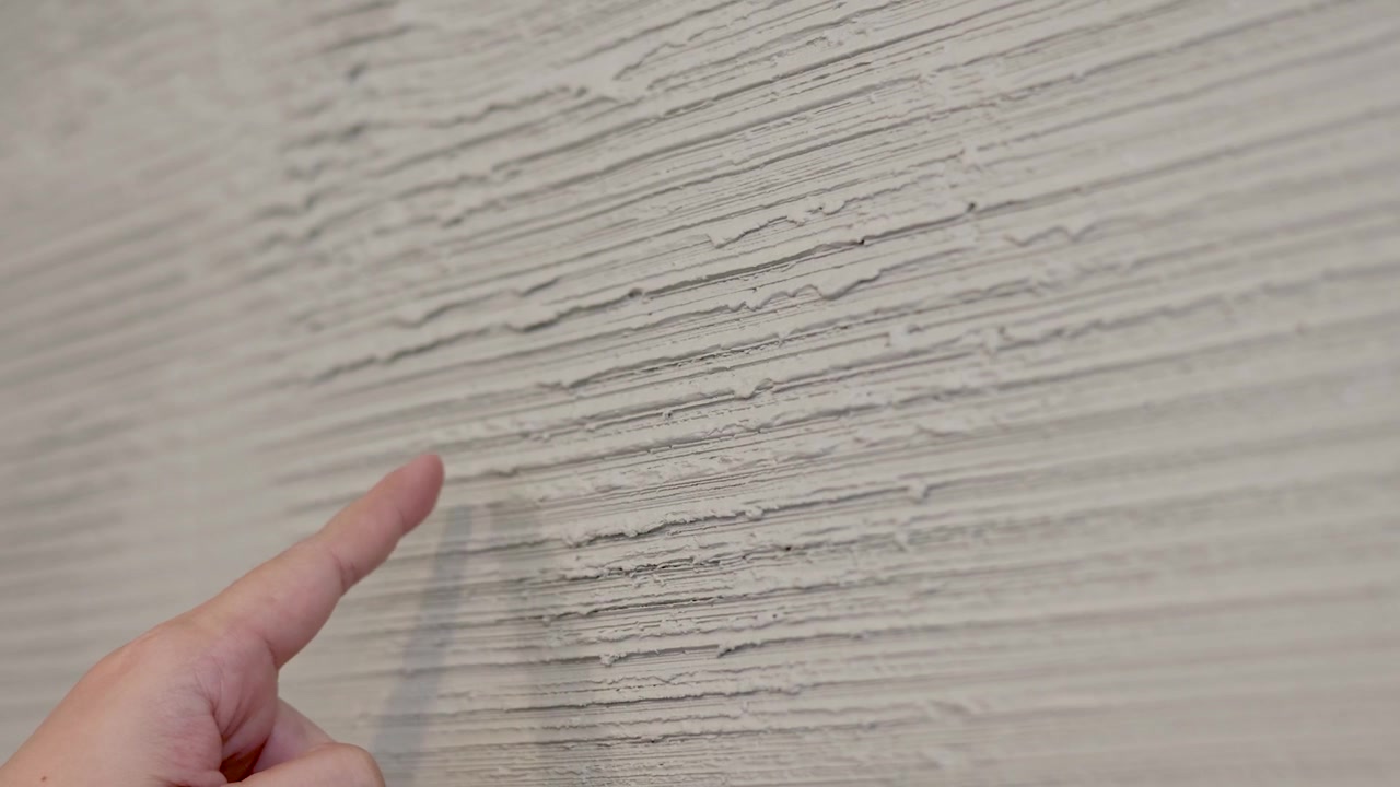 A person's finger points at and touches a rough, grey textured concrete wall surface