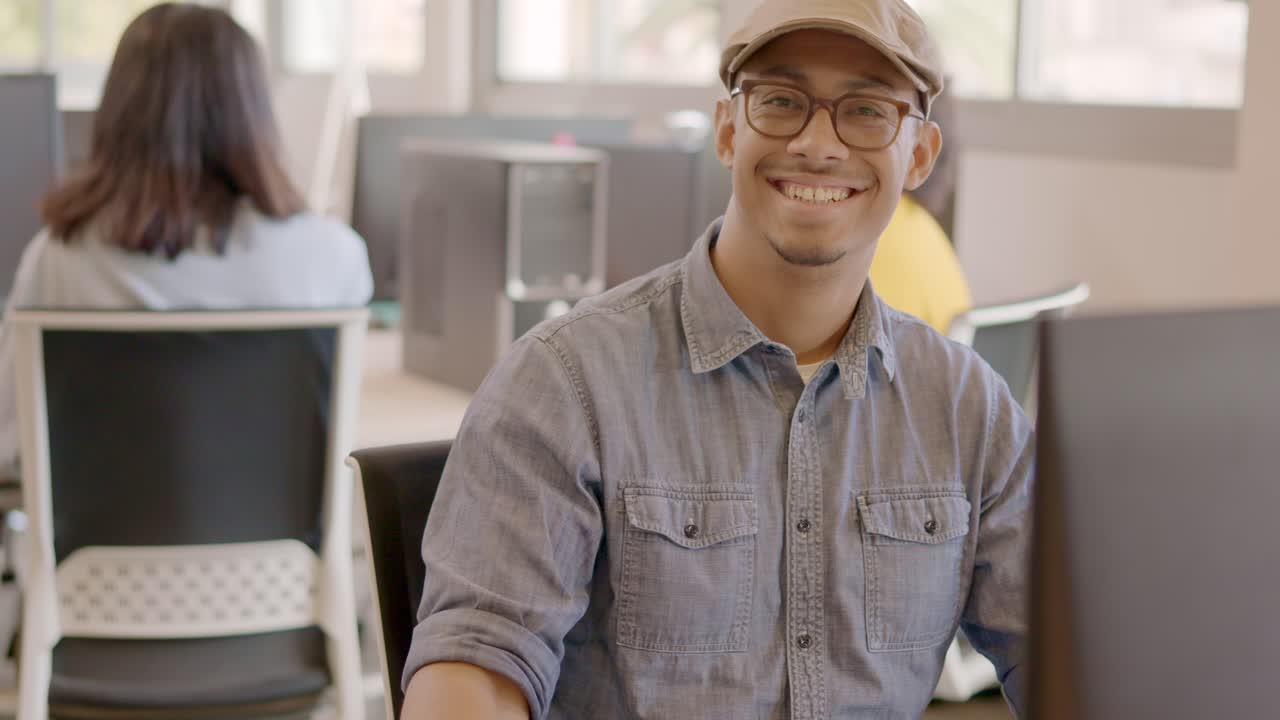 Productive man using computer and then smiling in a coworking