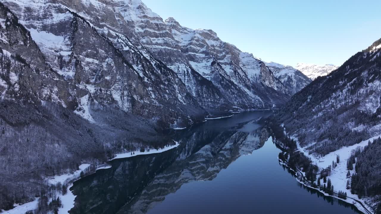 Vista aerea mozzafiato del Klöntalersee in inverno, circondato dalle cime innevate delle Alpi glaronesi, Svizzera, riflessi limpidi del lago, splendida scena alpina