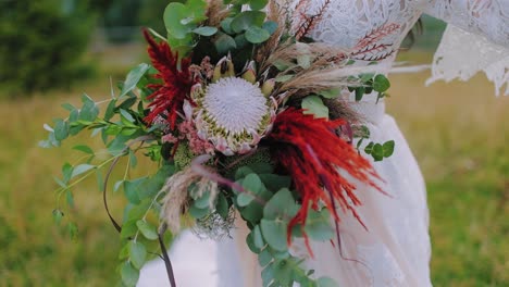 bouquet of exotic flowers in woman's hands. bride in wedding white dress holding wild flowers among nature in summer. close-up.