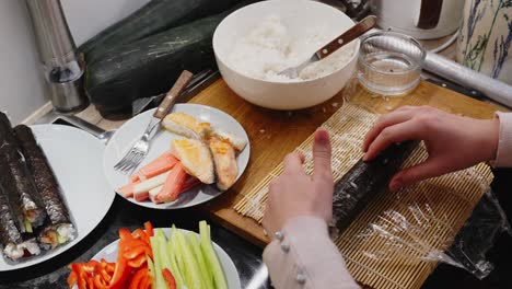 signora che rotola sushi verde su stuoia di legno, preparazione fatta in casa