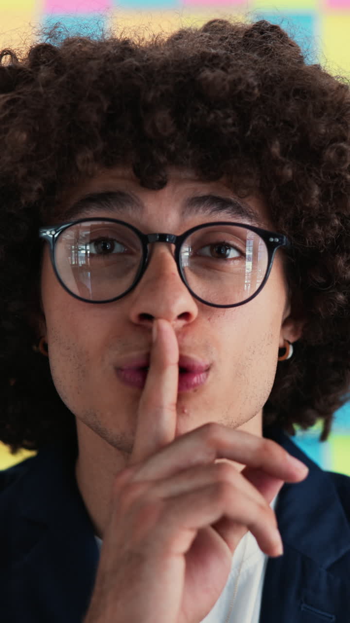 Young Man with Curly Hair Gestures for Silence with Finger on Lips