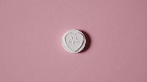 mano recogiendo caramelos de corazón con todo tu mensaje sobre fondo rosa