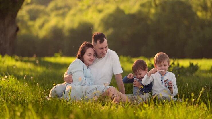 genitori amorevoli abbracciati seduti nel campo al tramonto e guardando sorridendo a due figli che mangiano gelato in estate.