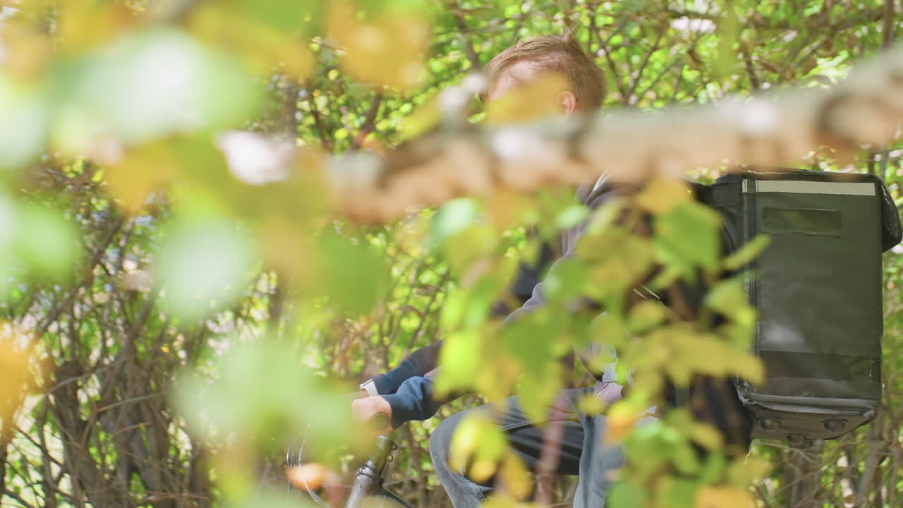 white male courier riding suburban path, delivering groceries from local shop in insulated pack, relaxed cadence under leafy canopy, morning light and dappled shadows, neighborhood route with app