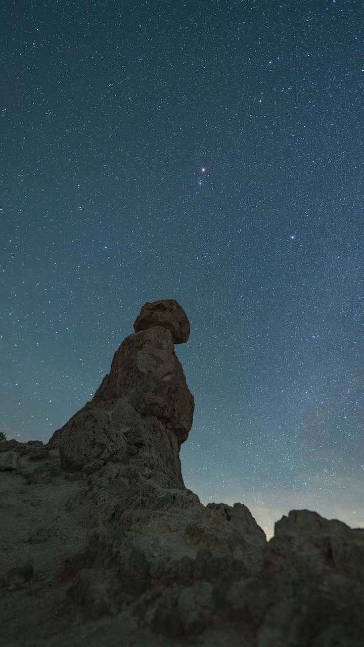 A panning right, vertical night timelapse of the starry sky across a rocky desert pinnacle foreground