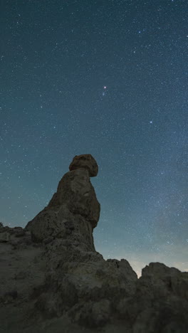 a panning right, vertical night timelapse of the starry sky across a rocky desert pinnacle foreground