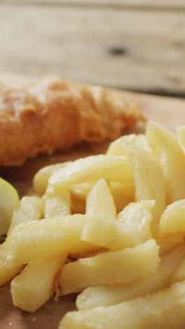 video of fish and chips with lemon wedge on wooden board, on rustic table