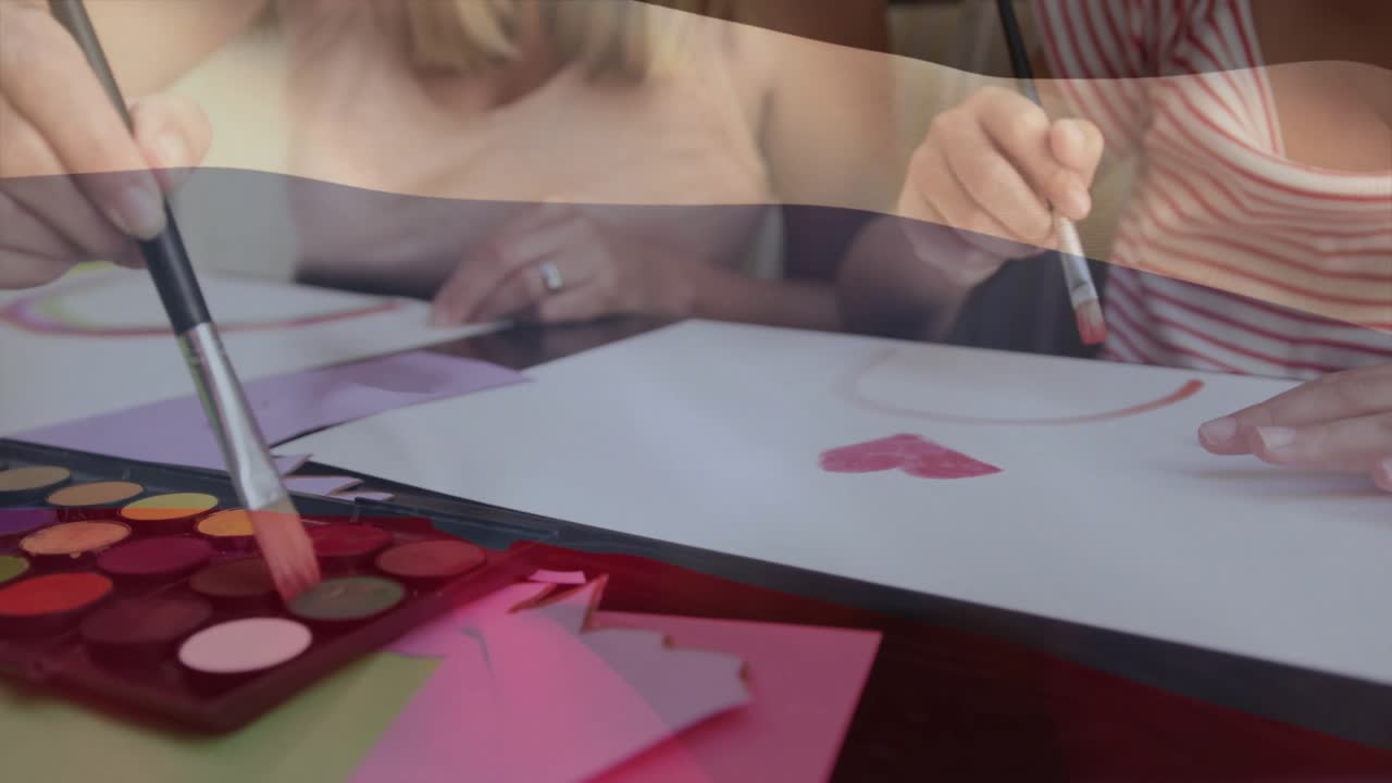 Madre sumergiendo un pincel en pintura roja y guiando a su hija pintando formas de corazón para la educación artística.