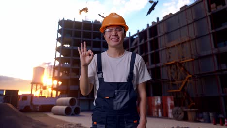 un trabajador asiático muestra un gesto de "okay" a la cámara en el sitio de construcción.