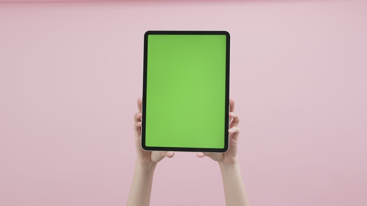 손으로 디지털 태블릿을 들고 크로마 키 스크린과 분홍색 배경에 표시합니다.