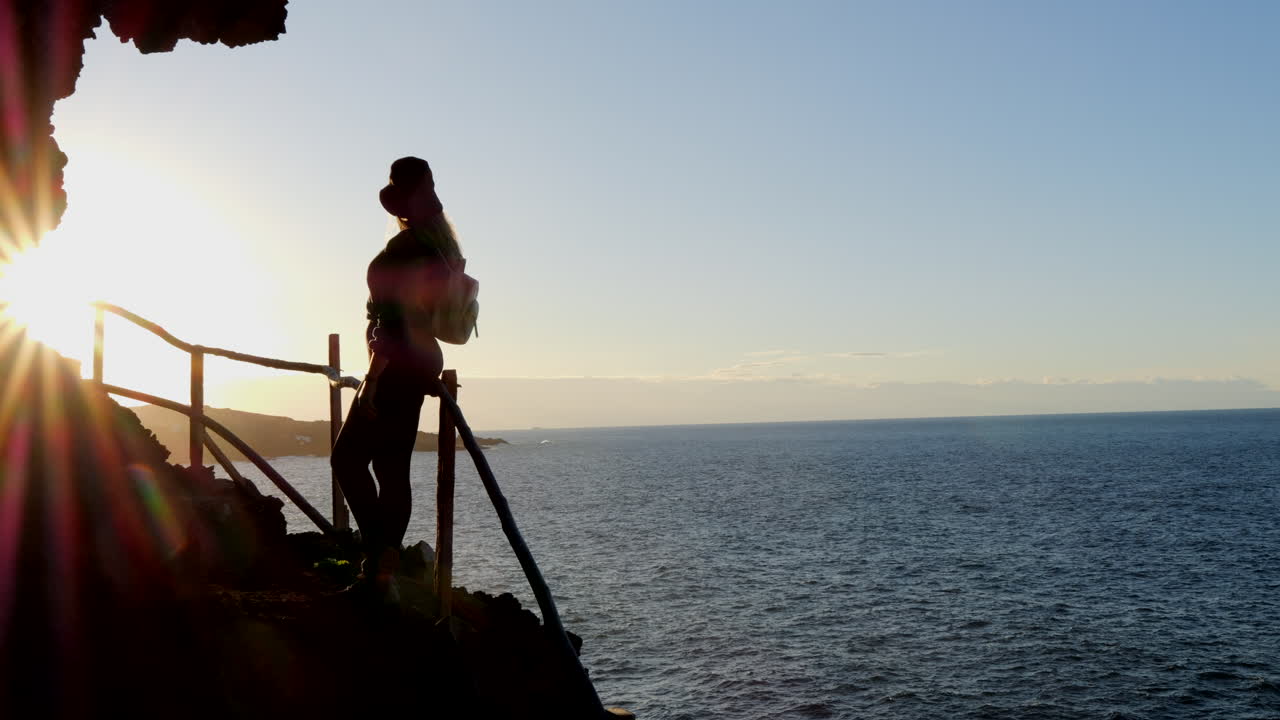 Magnifica ripresa di una giovane donna con cappello che ammira al tramonto il paesaggio della costa del comune di Gáldar sull'isola di Gran Canaria.