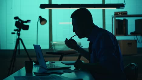 medium silhouette video of a detective policeman sitting in the interrogation room smoking working medium silhouette video of a detective policeman sitting in the interrogation room smoking working on a laptop and studying a knife from the evidence true crime documentary creative content