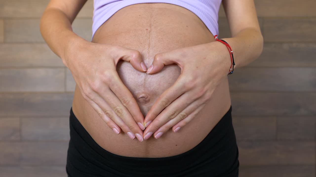 Donna incinta forma un cuore con le mani sulla pancia grande, primo piano.