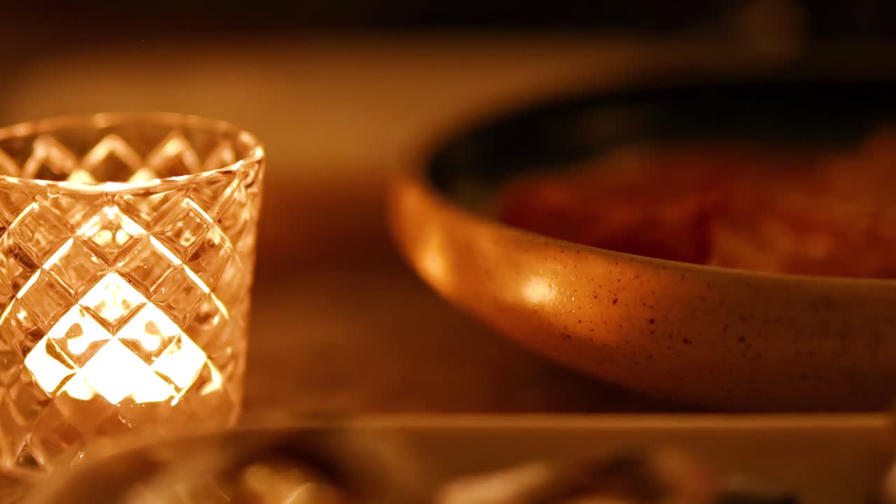 A warm candle illuminates a textured glass and a ceramic bowl, creating a cozy ambiance.