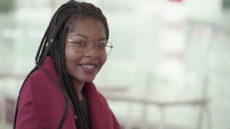 vista lateral de una joven afroamericana atractiva con labios rosados y trenzas en gafas de aviador con abrigo rosado