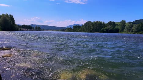 a tranquil river scene with flowing water and lush greenery beneath a bright blue sky, showcasing the beautiful natural landscape and serene atmosphere