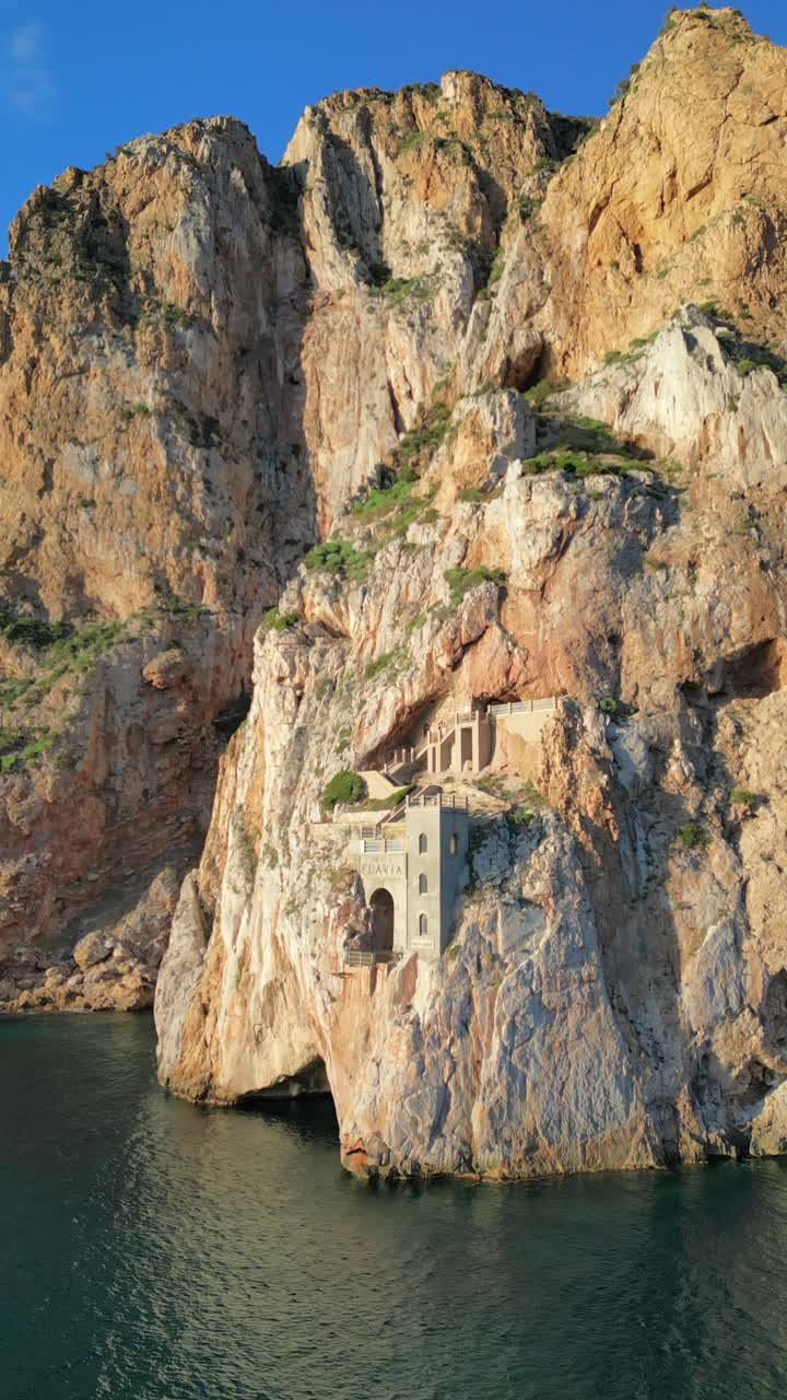 drone shot of Porto Flavia in Sardinia. Showing the face of the port from above the sea in front of it. Sunny day with no overcast. Water is calm but with visible