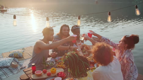 happy friends toasting at dinner party table on lake pier