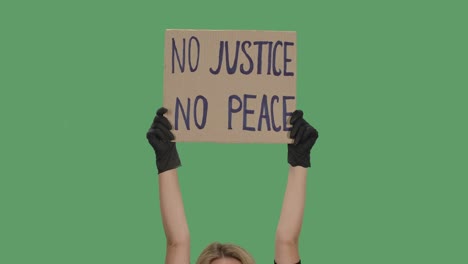 the hands of an unknown person in black gloves raise a cardboard poster no justice no peace. equality and unity concept. isolated a green screen, chroma key. close up. slow motion