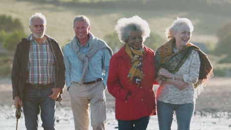 group of senior friends walking along shoreline of autumn beach