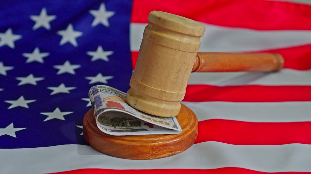 Martello di legno che colpisce una banconota da un dollaro statunitense su un blocco sonoro, su sfondo di bandiera americana