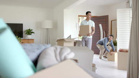 happy diverse gay male couple carrying packing boxes into new home, copy space, slow motion