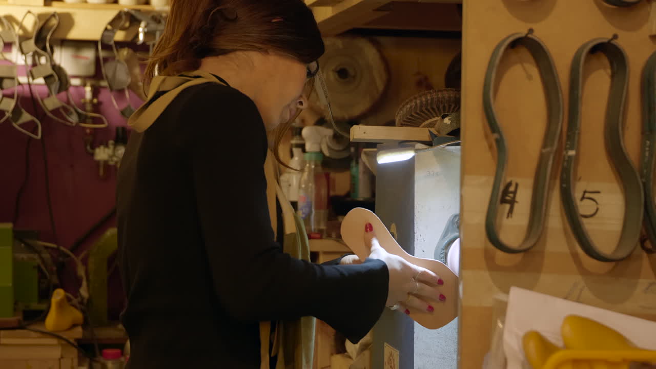 hembra usando maquinaria de pulido de suela antigua en taller de zapateros, vista lateral