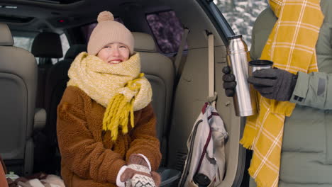 teenage girl dressed in winter clothes sitting in the trunk of a car while talking with her parents