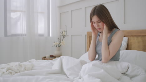 Women-sitting-on-bed-holding-her-head.-She-has-a-painful-headache.-The-woman-experiences-a-headache-rubs-her-temples-and-frowns-in-pain.-Seasonal-disease-Caucasian-girl-in-the-bedroom-on-sick-leave