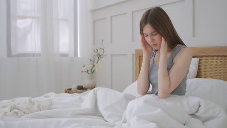 침대에 앉아 머리를  ⁇ 고 있는 여성. 그녀는 고통스러운 두통을 겪고 있습니다. 여성은 두통을 경험합니다. 그녀의  ⁇ 이를 문지르고 통증으로 눈살을  ⁇ 푸립니다. 계절성 질병 백인 소녀는 병원에서 침실에 있습니다.
