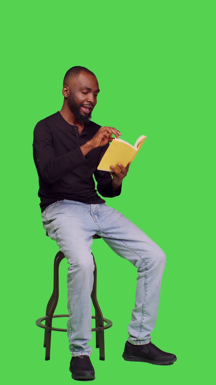 Vertical video: Side view of male model reading novel story on book in studio