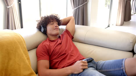 a young biracial man relaxes on a sofa at home with headphones