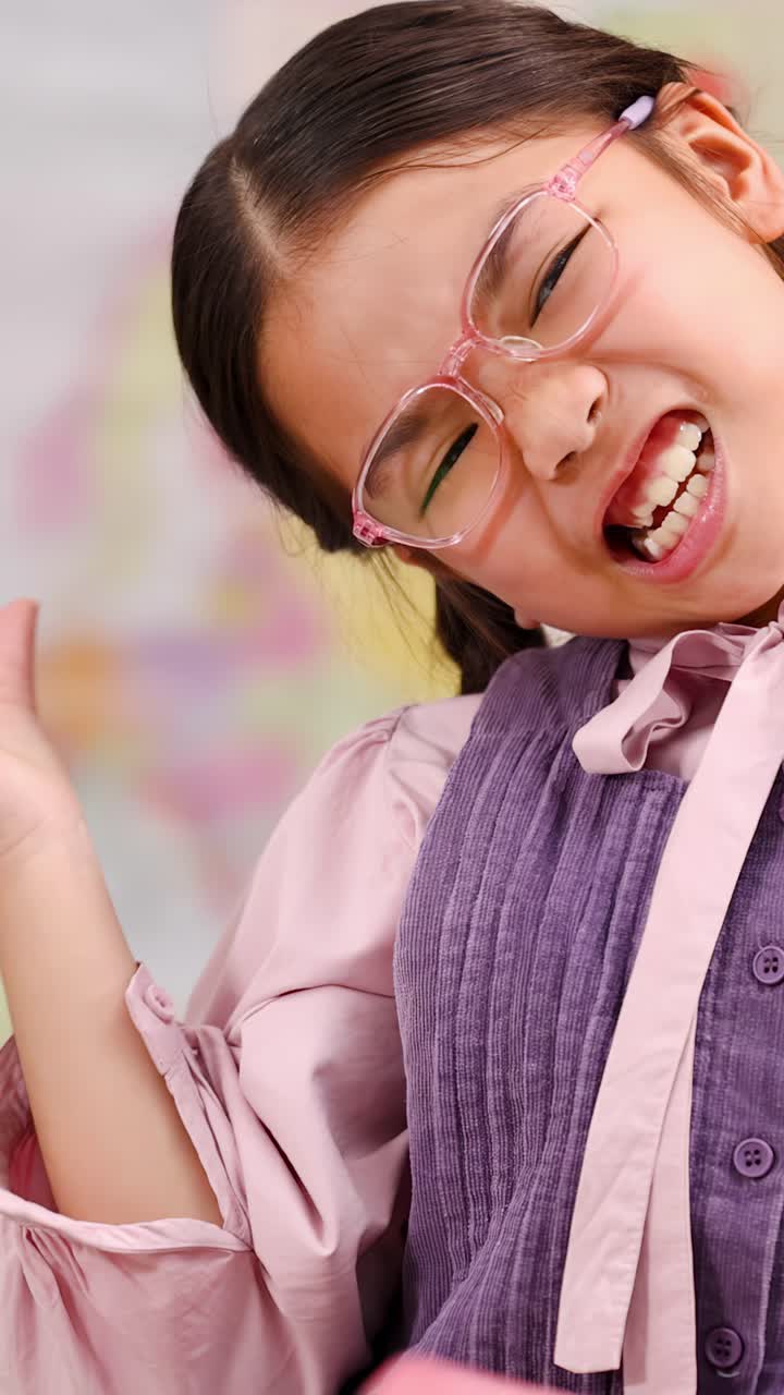 Confident schoolgirl in pink glasses poses playfully against a colorful classroom background with pencils
