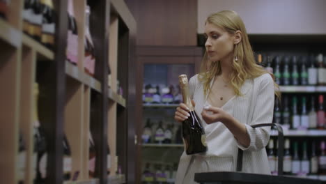 the girl buys wine in the store reading the labels on the bottle and choosing a supermarket alcoholic beverage on the wine shelf.