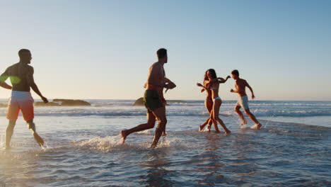 Grupo-De-Amigos-Corren-Juntos-A-Través-De-Las-Olas-En-Vacaciones-En-La-Playa