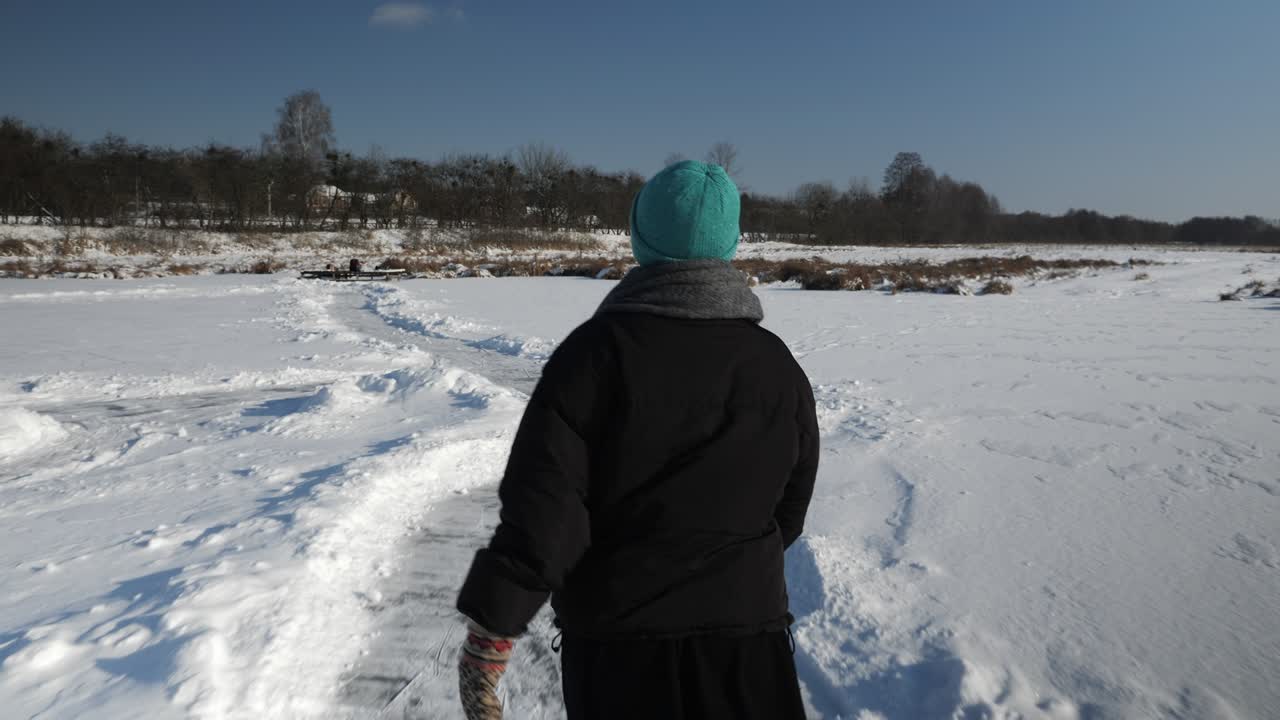 Tracking shot of woman ice skating on ice on river. Female in winter outfit is skating on frozen lake. Winter sport activities