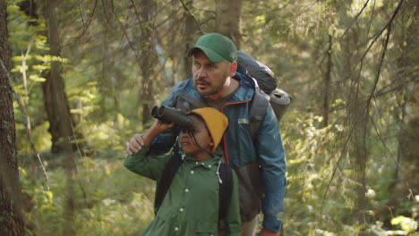 father and son using binoculars in woods