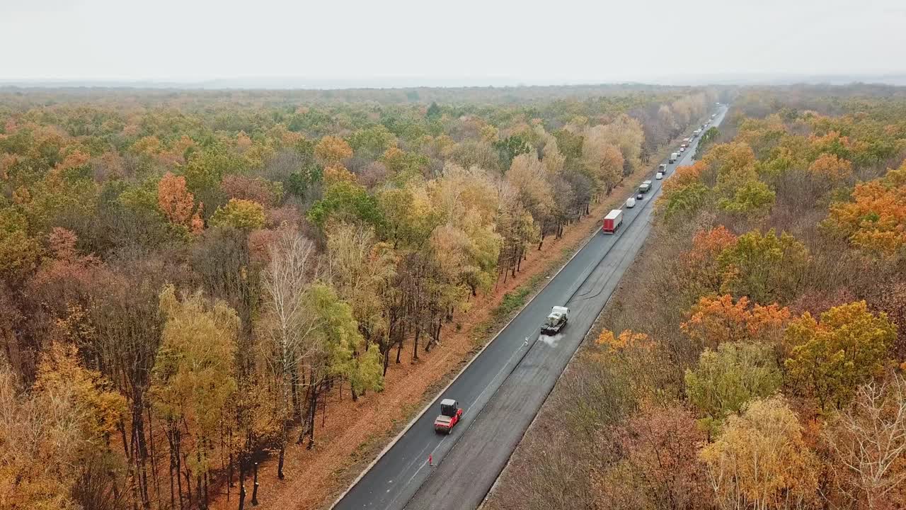 Aerial view of asphalt road in the forest. Cars moving in one side on road among autumn trees. Road trip through fall forest.