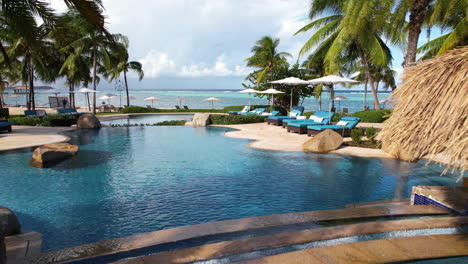 Flying-Above-Swimming-Pools-of-Luxury-Caribbean-Beachfront-Resort-With-Beach-and-Sea-in-Background,-Drone-Shot