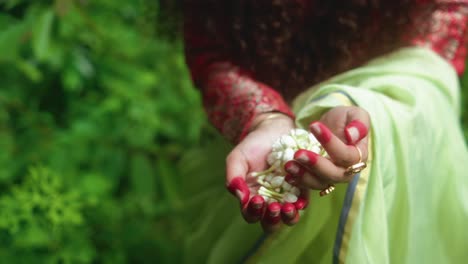 close-up of hands with red-painted nails gently holding white flower petals in green outdoor setting
