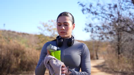 joven caucásica en ropa deportiva limpiando el sudor y bebiendo agua al aire libre en un día soleado.