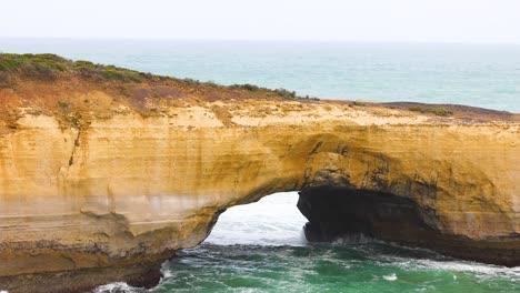 a serene view of the natural arch formation at london bridge, port campbell, with ocean waves and soft lighting
