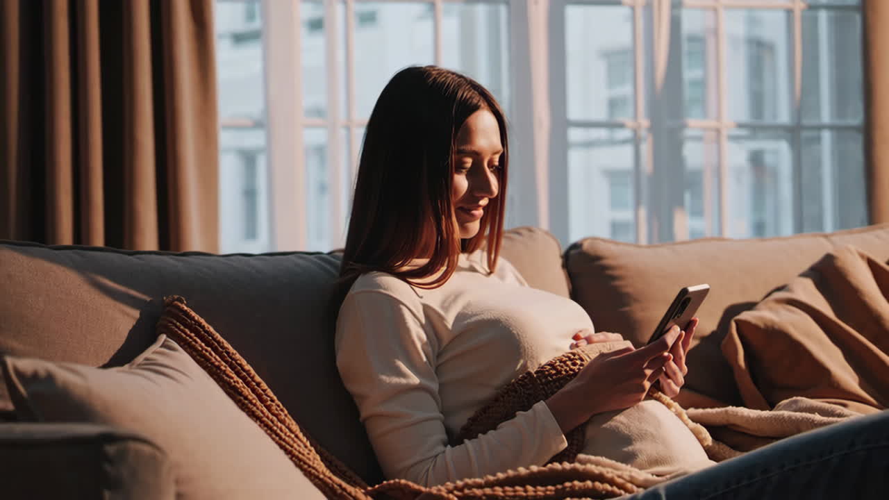 Pregnant woman using smartphone on sofa