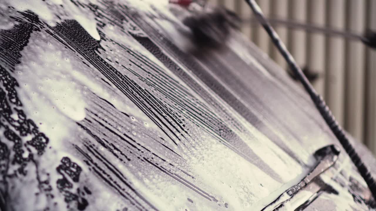 Washing car window with cleaning brush, white foam closeup view