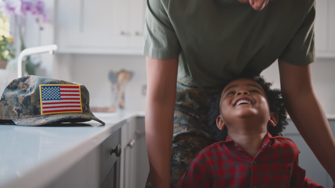 madre del ejército estadounidense en uniforme en casa de licencia jugando con su hijo en la cocina de la familia