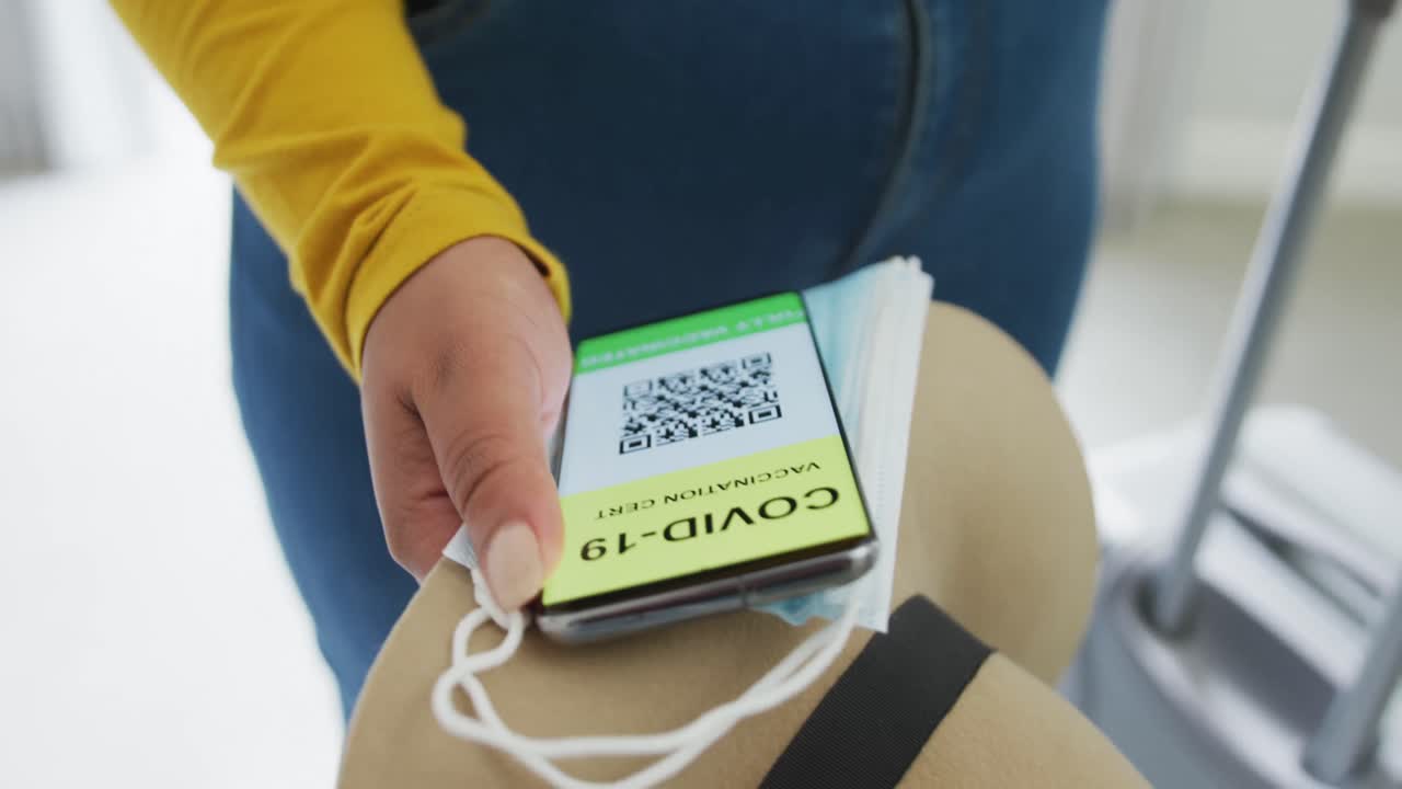 mujer afroamericana de talla grande que sostiene un teléfono inteligente con pasaporte covid y máscaras faciales